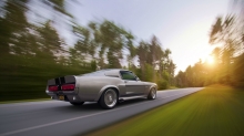 Серебристый Ford Mustang Eleanor устремляется к солнцу на лесной трассе